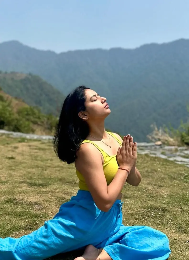 Pooja in a seated pose with hands in prayer on a Himalayan hillside